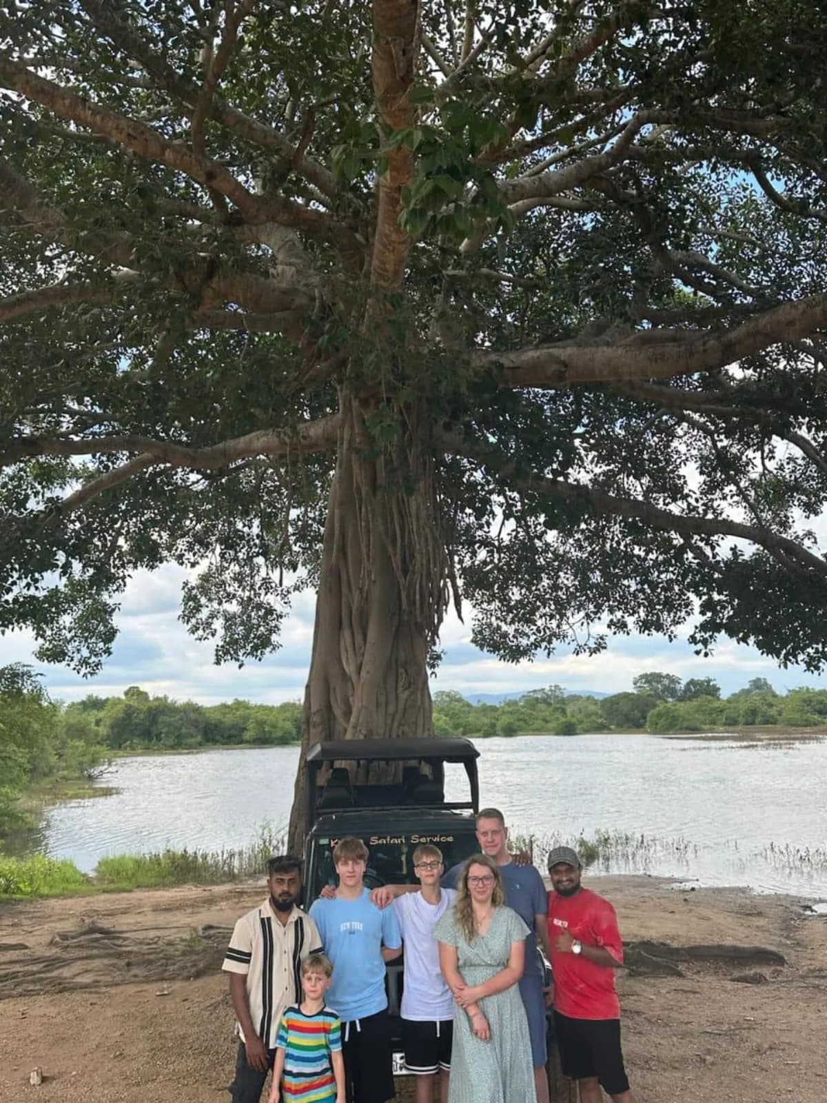 A family and their jeep beneath a huge lakeside tree